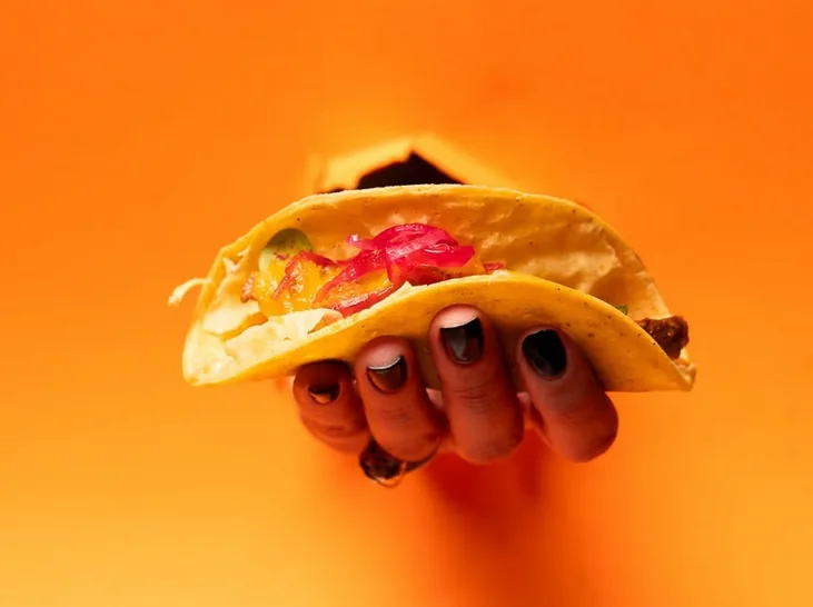 A hand holding a taco against a warm orange background.