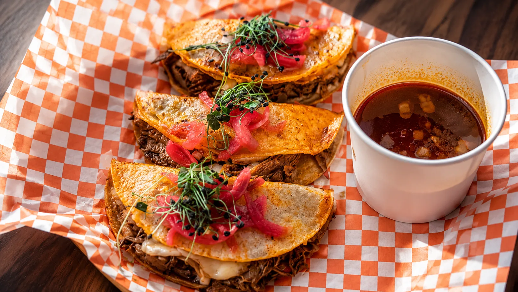 Tacos served with consomme on checkered paper.